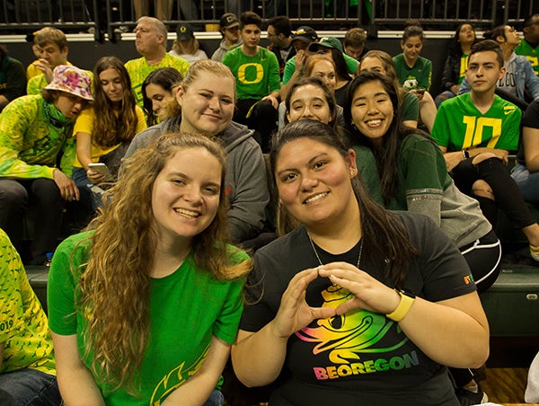 Students smiling at the camera dressed in UO fan gear watching an event.