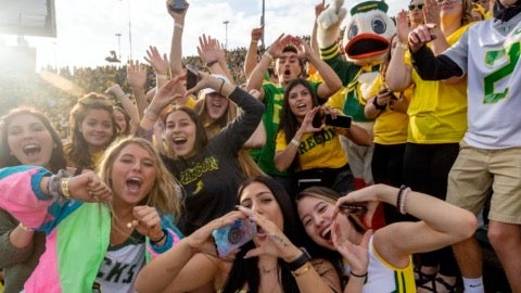 A crowd of students cheering at the camera with the UO Duck mascot in the background