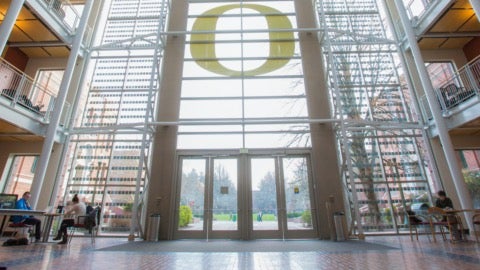 Looking outside from the lobby of a glass-front building, a yellow "O" logo over the door way