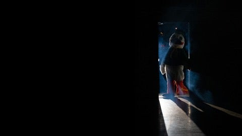 UO Duck mascot leaving a dark room through a spotlit doorway