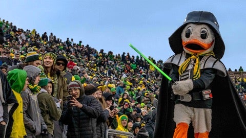 UO Duck mascot dressed in a Darth Vader costume, walking past a crowd of students