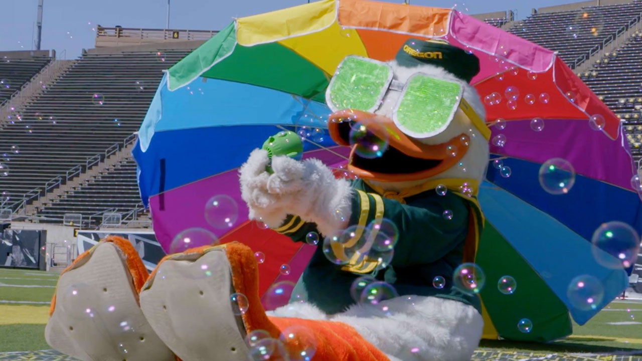 UO Duck mascot under rainbow umbrella and blowing bubbles