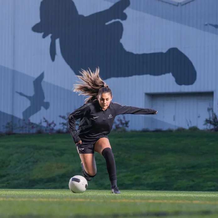 Student wearing a black 'Oregon' uniform plays soccer on the intramural fields nestled between the Student Recreation Center and Hayward Field.